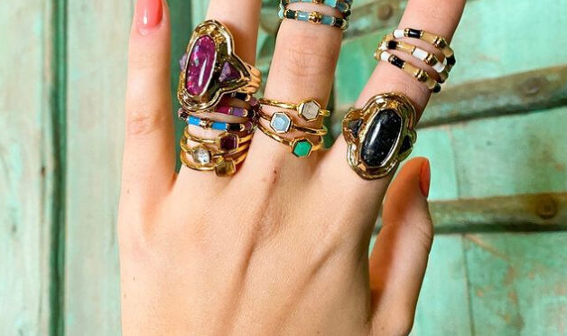 many rings stacked on three fingers of a hand on a green wood background